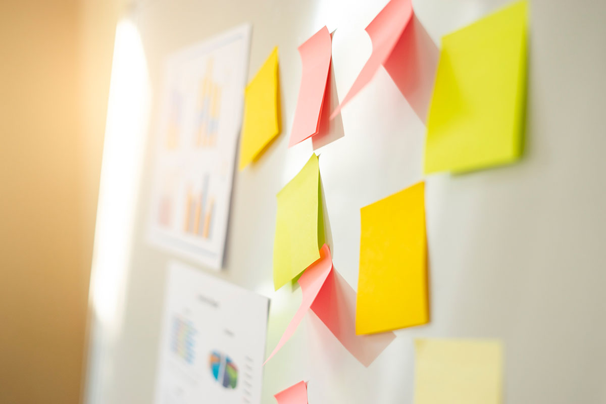 Colorful sticky notes and printed bar and pie charts pinned to a white wall in a sunlit office