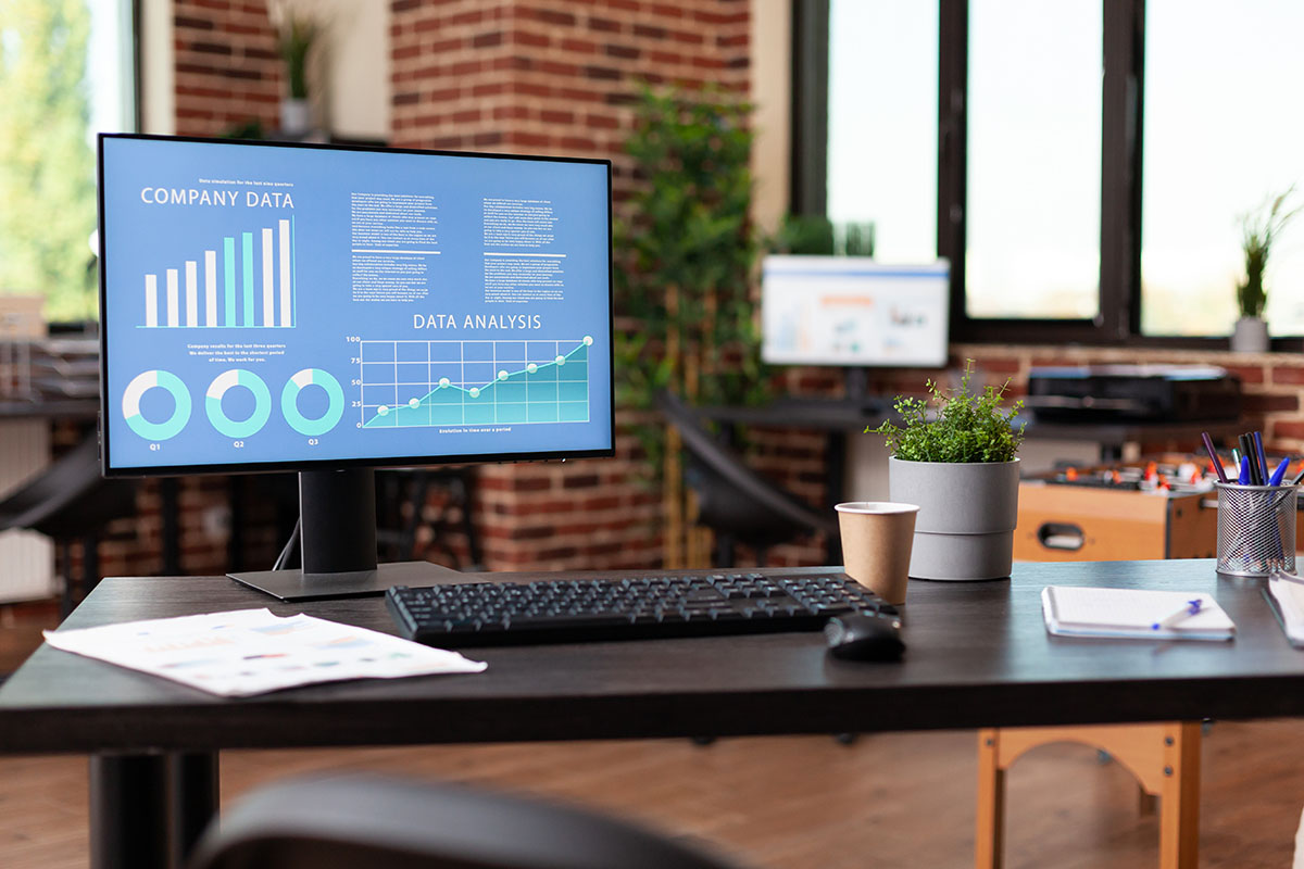 Desktop monitor showing company data charts on a desk in an empty modern office
