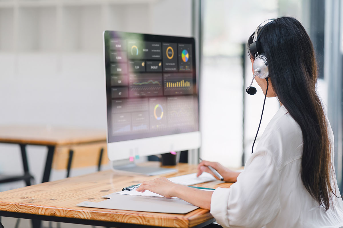 Customer service agent wearing a headset working in front of a monitor showing an analytics dashboard