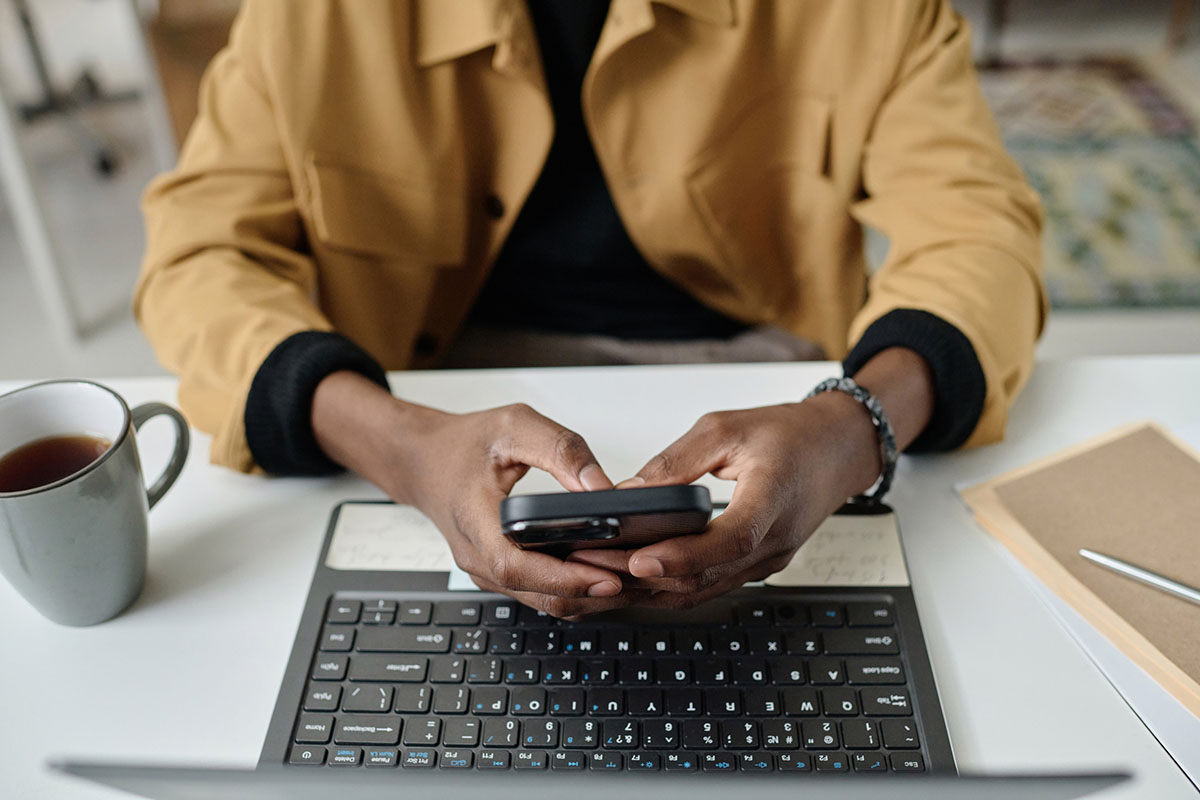 Close-up of an employee&rsquo;s hands typing on a smartphone above an open laptop on a white desk