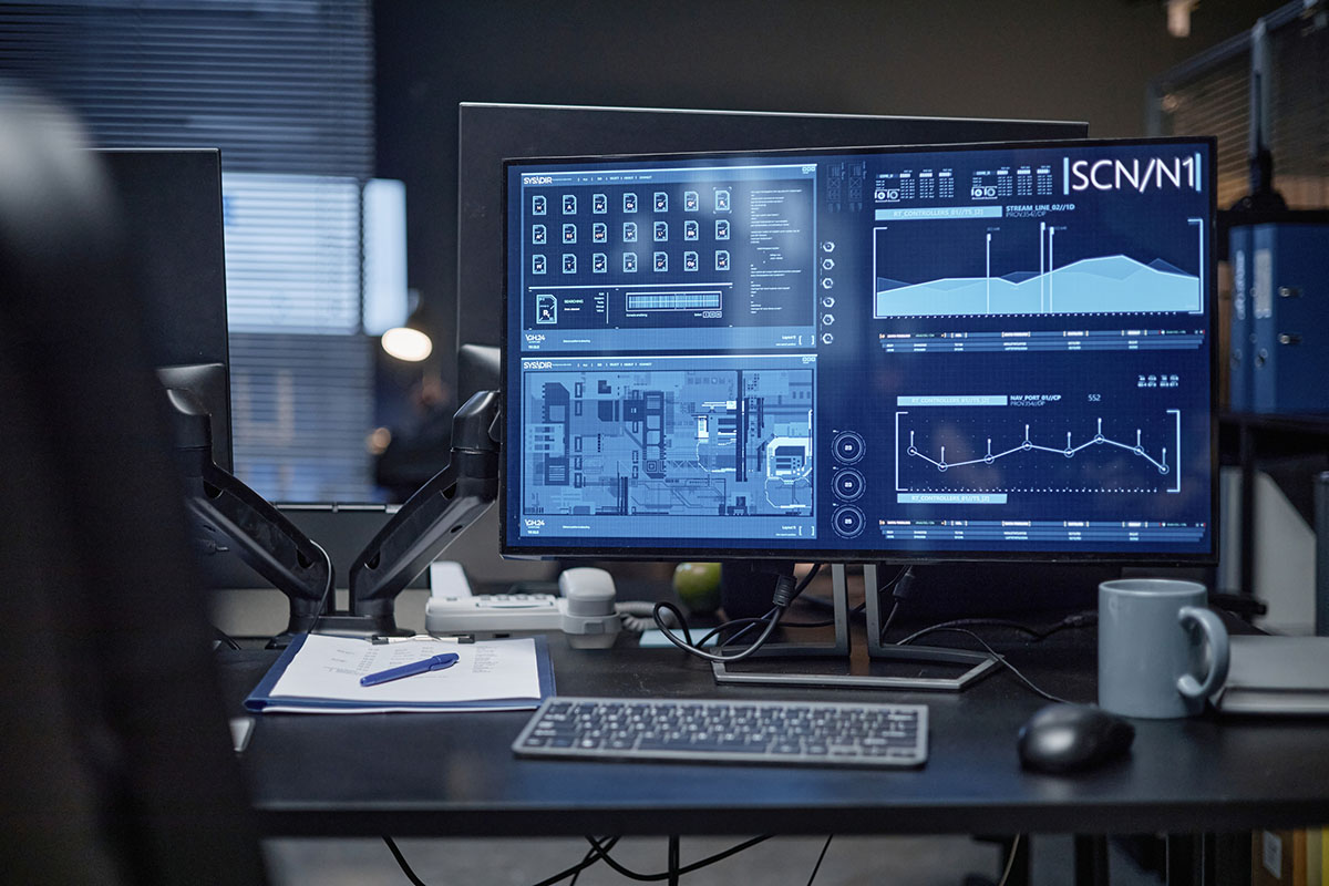Computer monitor displaying traffic analytics charts and system panels on a desk in a dimly lit operations office