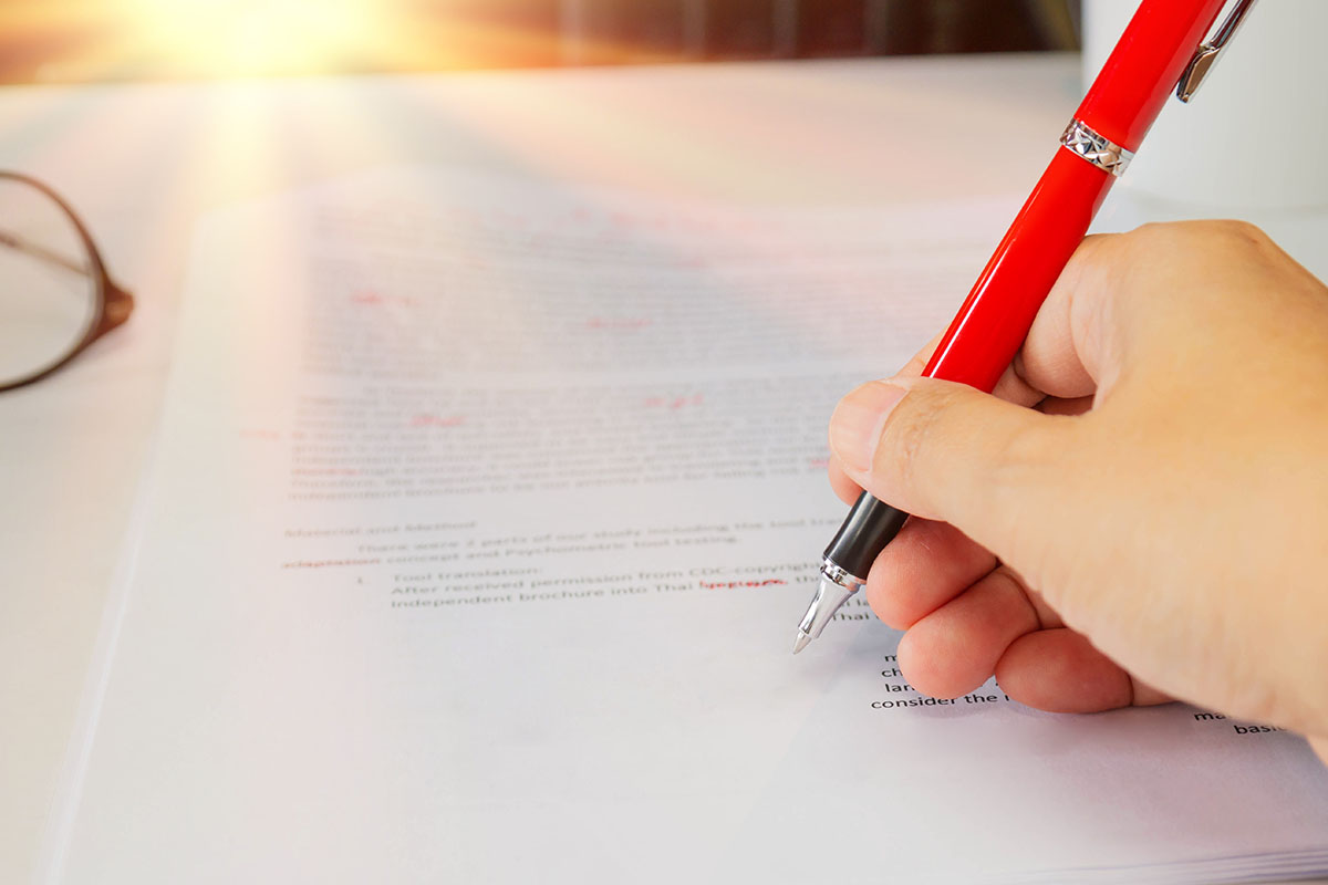 Close-up of a hand marking corrections in red pen on a printed document